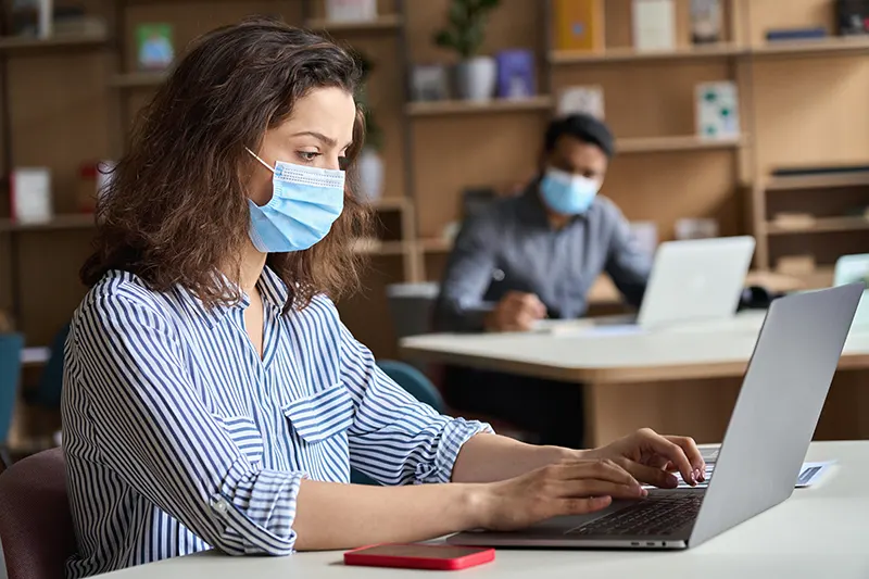 Professional woman employee in facemask working sitting at table. Occupational disease.