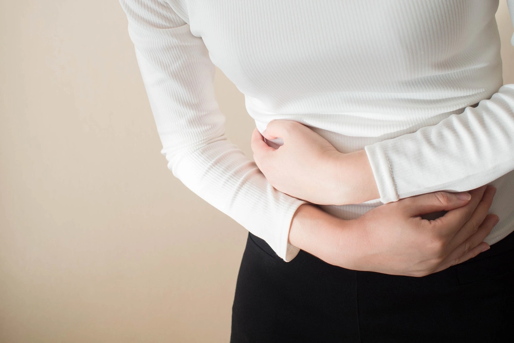 Young female suffering form stomach ache on gray background w/ copy space.