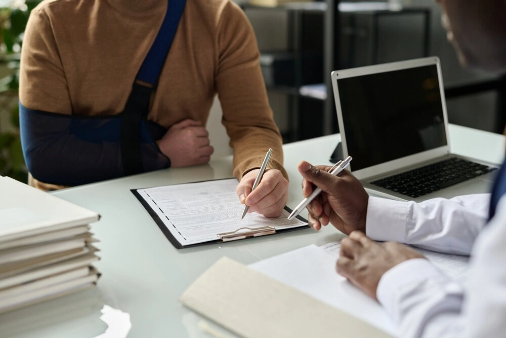 Close up of man filling in medical insurance form, injured hand in sling in background,