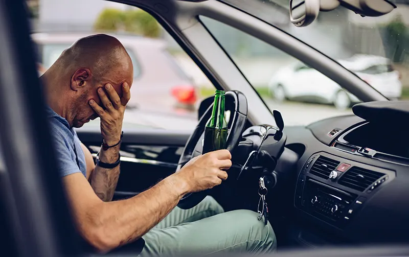 Drunk driver drinking alcohol in car and holding beer bottle