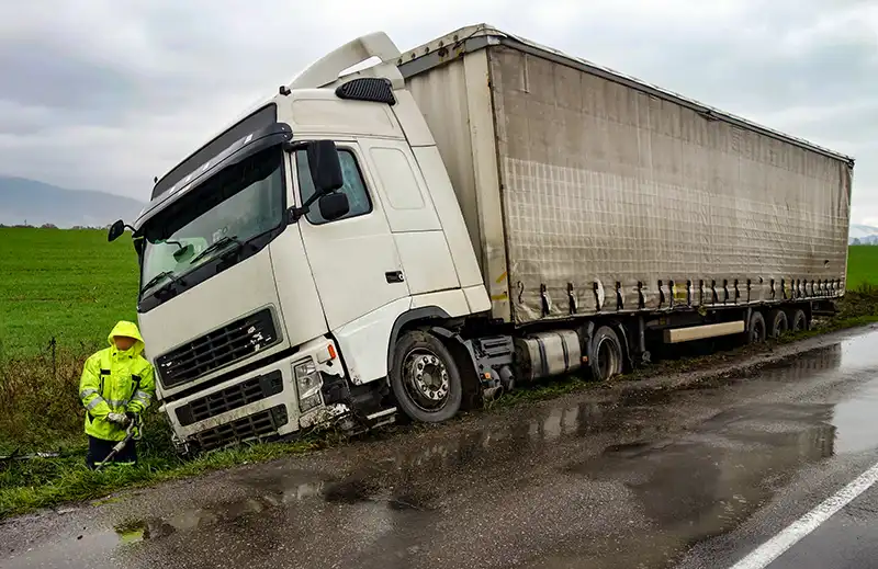 The truck lies in a ditch after the road accident over raining day in autumn time.