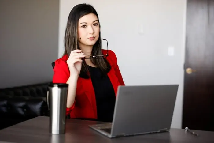 Woman holding eyeglasses with a laptop in front of her