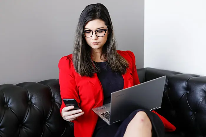 Woman sitting on a couch holding a phone and a laptop