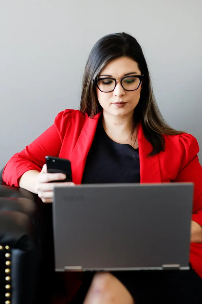 Woman sitting on a couch holding a phone and a laptop
