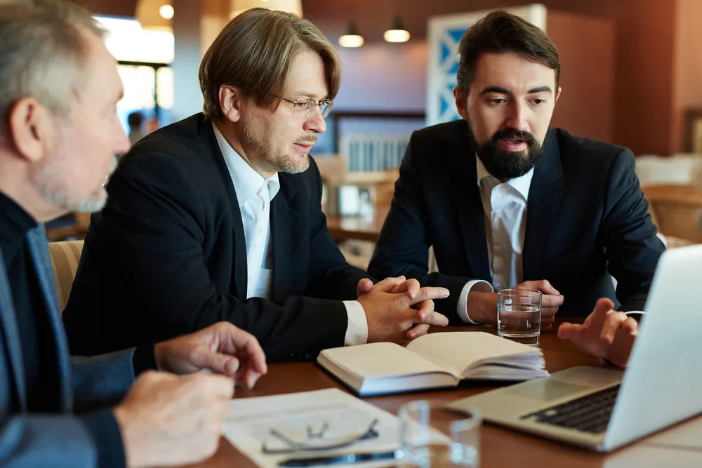 Teamwork of three bearded managers: they gathered together in cozy cafe and analyzing results of accomplished work, waist-up portrait